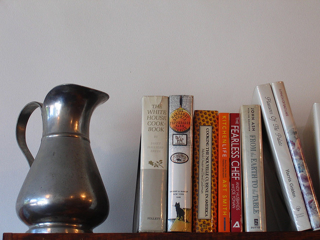 a stack of old cookbooks next to a silver serving vessel